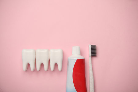 Plastic models of teeth and toothpaste tube, toothbrush on pink background. Dental care. Flat lay