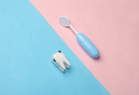Ttoy tooth affected by caries and dentist's mirror on blue-pink background. Dental treatment, visit to the dentistの写真素材