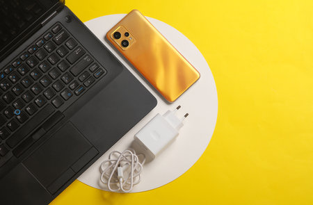Laptop with smartphone, cable and charging adapter on yellow background. Top view. Flat layの写真素材