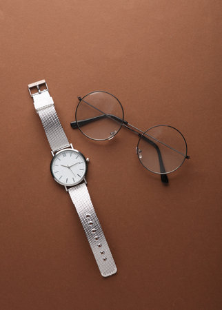 Stylish wristwatch with eyeglasses on a brown background. Women's accessories. Top viewの写真素材
