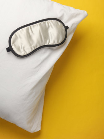 Sleeping mask with pillow on a yellow background. Healthy sleep conceptの写真素材