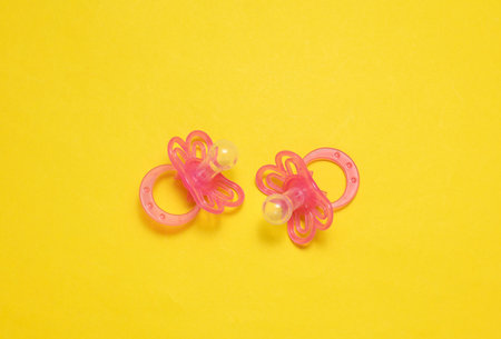 Two baby pacifiers on yellow background.