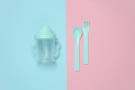 Drinking bowl and plastic fork and spoon for baby on a blue and pink background. Top viewの写真素材