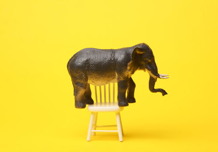 Toy elephant balancing on chair, yellow backgroundの写真素材