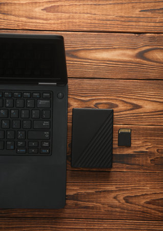 Laptop with external hard drive and sd card on wooden table