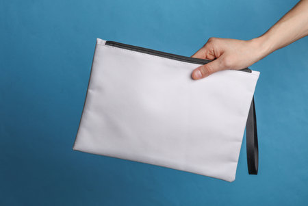 Female hand holding a mockup of a white fabric cosmetic bag on a blue backgroundの写真素材