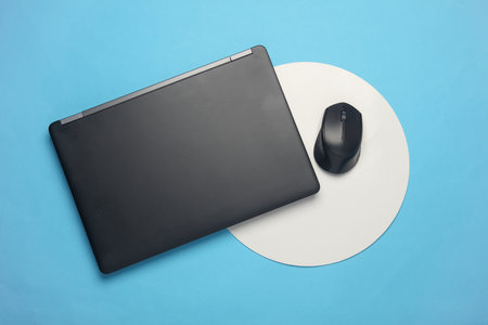 Laptop and pc mouse on blue background with white circle. Minimalism. Business conceptの写真素材