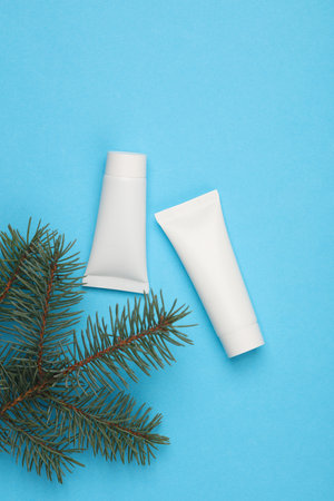 White cream tubes with pine branches on a blue background. Mockup for designの写真素材
