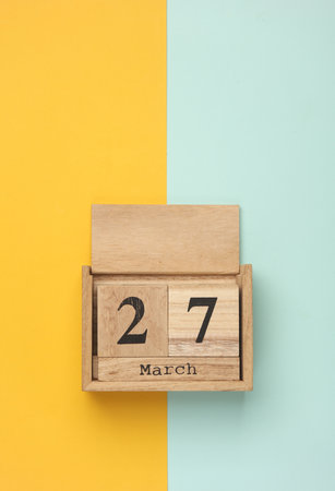 Wooden block calendar with date March 27 on blue yellow backround. Top view. Flat layの写真素材
