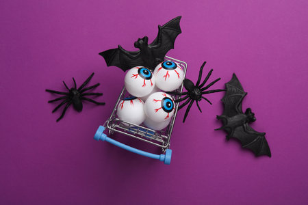 Minimalistic Halloween layout with eyeballs in a shopping cart, bats and spiders on purple backgroundの写真素材