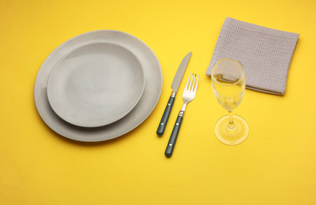 Plates, cutlery with towel, glass on yellow background. Table setting. Top viewの写真素材