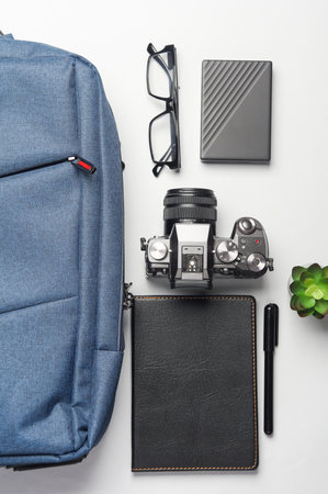 Backpack with photographer equipment and gadgets for work on white background. Flat lay. Top view