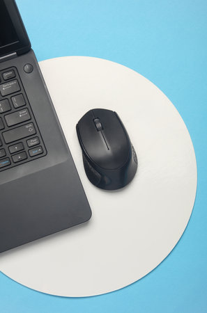 Laptop and pc mouse on blue background with white circle. Minimalism. Business concept