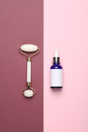 Massage roller and serum bottle for anti-aging facial massage on a pink burgundy backgroundの写真素材