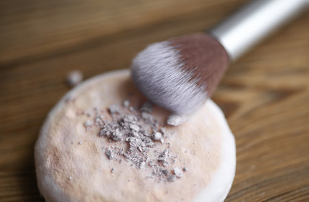 Makeup sponge with makeup powder and brush on a wooden background