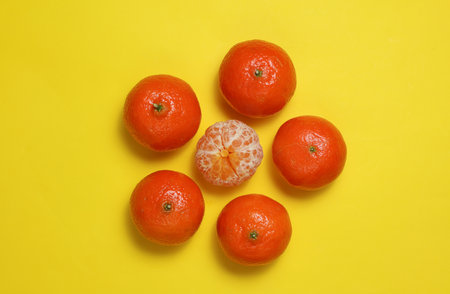 Peeled and unpeeled tangerine on a yellow background