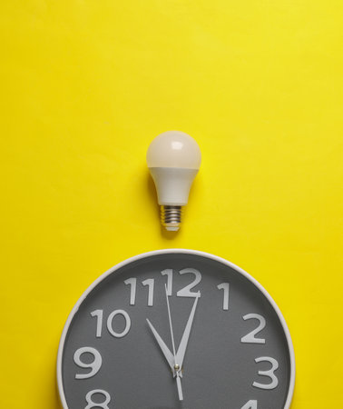 Large round clock with light bulb on yellow background. Creative idea, business conceptの写真素材
