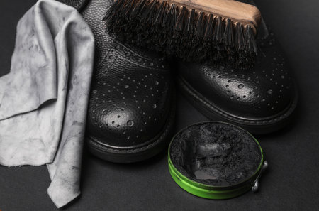 Black brogue boots with wax, rag and brush on black background. Leather shoes care