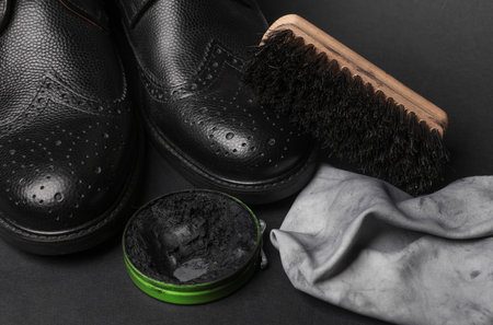 Black brogue boots with wax, rag and brush on black background. Leather shoes careの写真素材