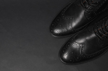 Stylish black leather men's brogue boots on a black background