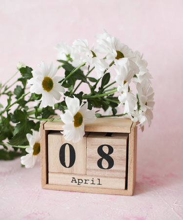April 8 date on wooden calendar with bouquet of flowers on pink concrete backgroundの写真素材