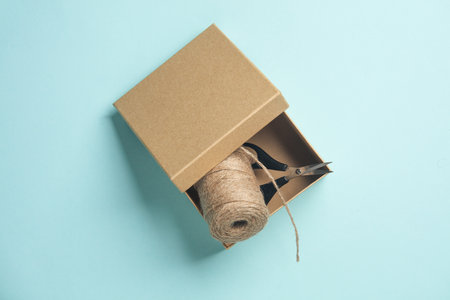 DIY, Product packaging, presentation. Kraft cardboard box with scissors and thread on a blue...