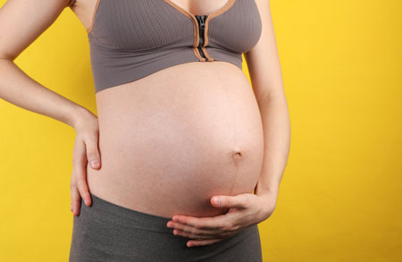 Pregnant woman holding her belly on yellow background