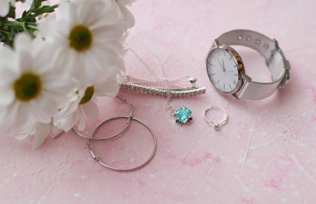 Silver jewelry or costume jewelry for woman and flowers on pink concrete background