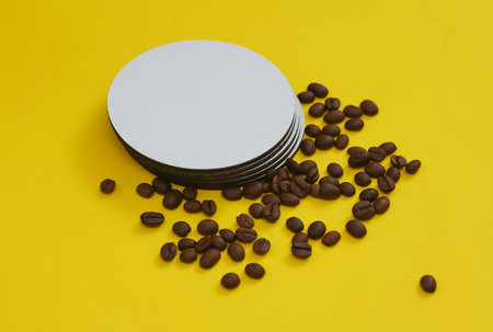 Mockup of white empty coasters for glasses or cups with coffee beans on a yellow backgroundの写真素材