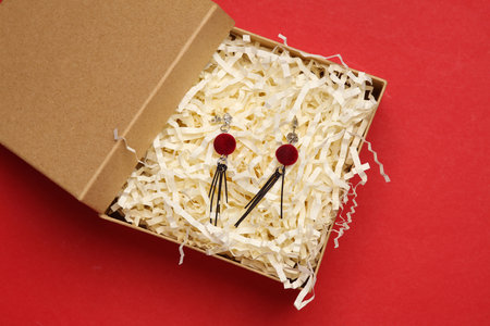 Earrings in craft box with filler on red background. Product packaging