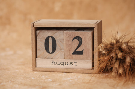 Wooden block calendar with the date August 02 and spikelets of wheat on a beige concrete backgroundの写真素材