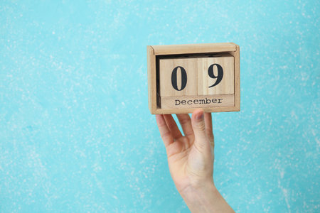 woman's hand holds wooden block calendar with the date December 09 on blue concrete background