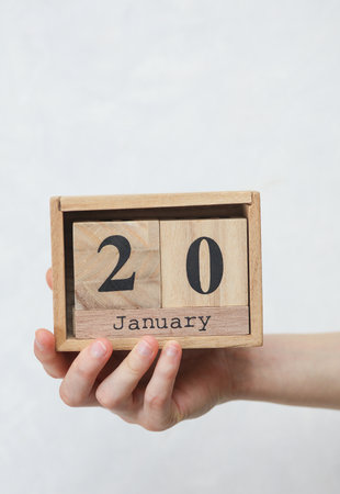 Woman's hand holds wooden block calendar with the date January 20 on white concrete backgroundの写真素材