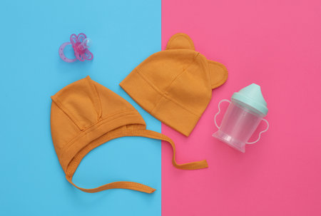 Newborn baby hats and pacifier, bottle on blue pink background