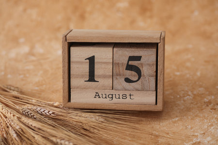 Wooden block calendar with the date August 15 and spikelets of wheat on a beige concrete backgroundの写真素材