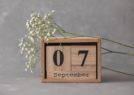 Wooden calendar with the date September 07 and gypsophila flowers on a gray concrete background