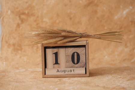 Wooden block calendar with the date August 10 and spikelets of wheat on a beige backgroundの写真素材