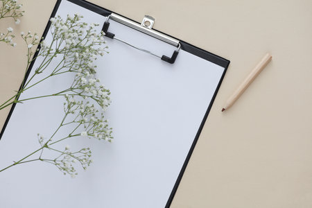 Clipboard with pencil and gypsophila flowers on beige backgroundの写真素材