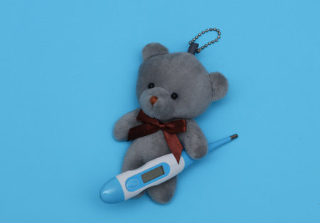Toy bear with an electronic thermometer on a blue background. Pediatric medicineの写真素材