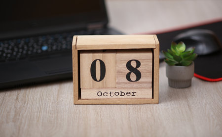 Wooden calendar with the date October 08 on a desktop with a laptopの写真素材
