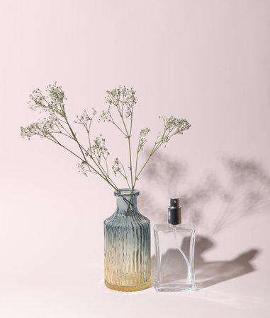 Perfume bottle and Glass vase with gypsophila flowers on a beige background with shadowの写真素材