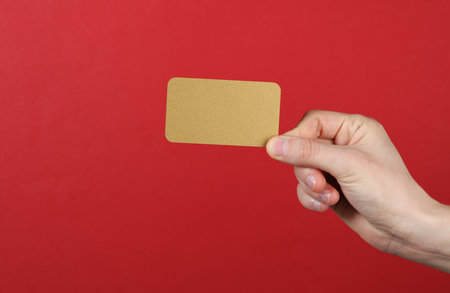 Hand holding golden bank card on red background