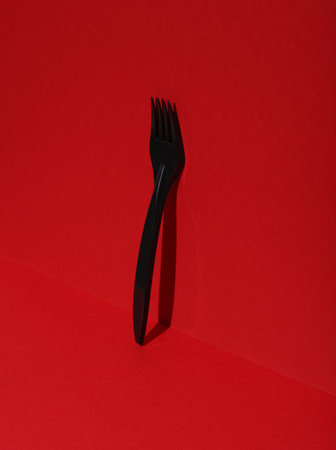 Black plastic fork on a red background with shadow. Creative layout
