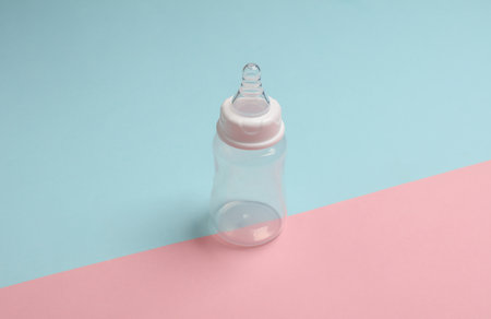 Bottle with nipple for feeding a newborn on a blue-pink backgroundの写真素材