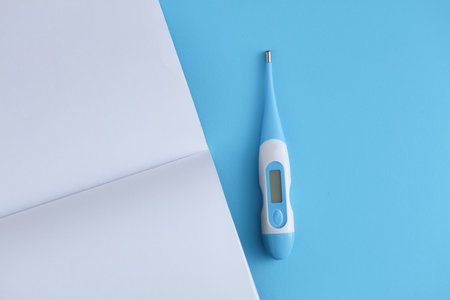Electronic thermometer with a blank open notebook on a blue background. Medicine conceptの写真素材