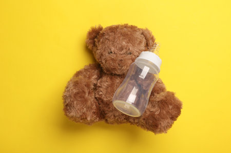 Toy bear holding Bottle for feeding newborn on yellow backgroundの写真素材