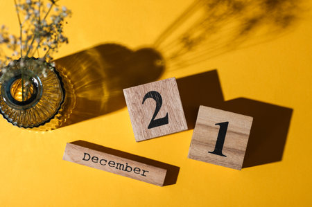 Wooden calendar with the date December 21 and flower in vase. Yellow background. Top viewの写真素材