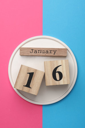 Wooden block calendar with the date January 16 in plate on pink blue background. Top viewの写真素材