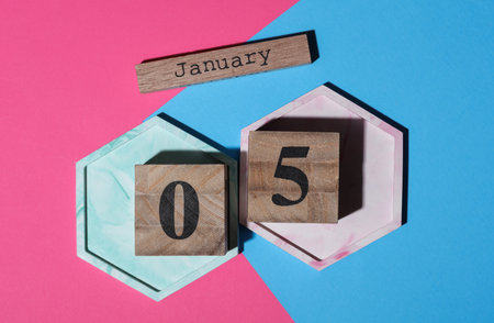 Wooden block calendar with the date January 05 on pink blue background. Top view