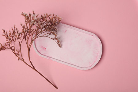 Oval plaster tray with dry flowers on a pink background. Top view